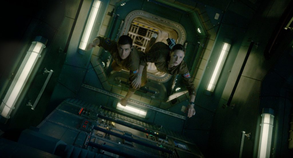 Jake Gyllenhaal and Rebecca Ferguson as two astronauts floating through a corridor in the International Space Station